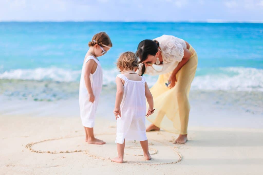 Une maman et ses filles traçant un cœur dans le sable sur la plage