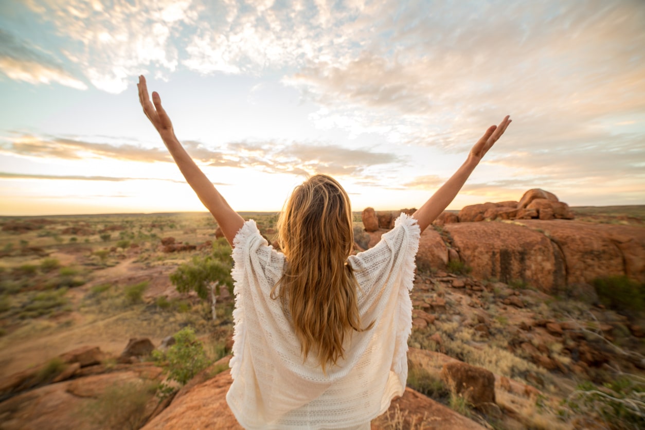 Jeune femme levant les bras au ciel face à l'immensité de Devil's Marble