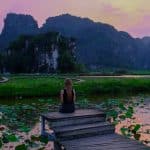 jeune femme face aux montagnes devant une étendue d'eau au coucher du soleil