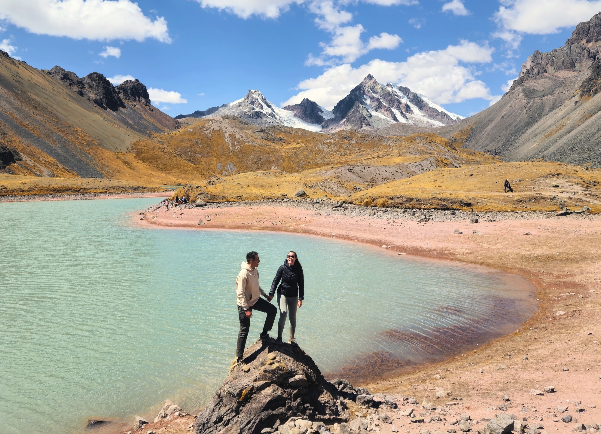 Couple sur un rocher main dans la main face à un lac de montagne