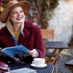 Jeune femme souriante assise à la terrasse d'un café en train de lire un magazine