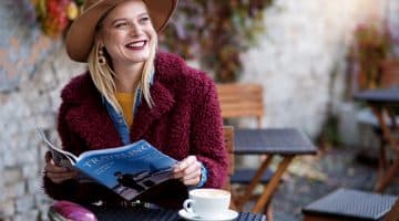 Jeune femme souriante assise à la terrasse d'un café en train de lire un magazine