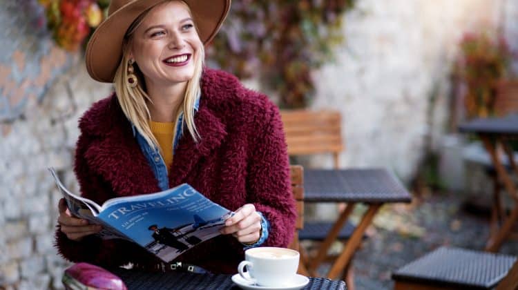 Jeune femme souriante assise à la terrasse d'un café en train de lire un magazine