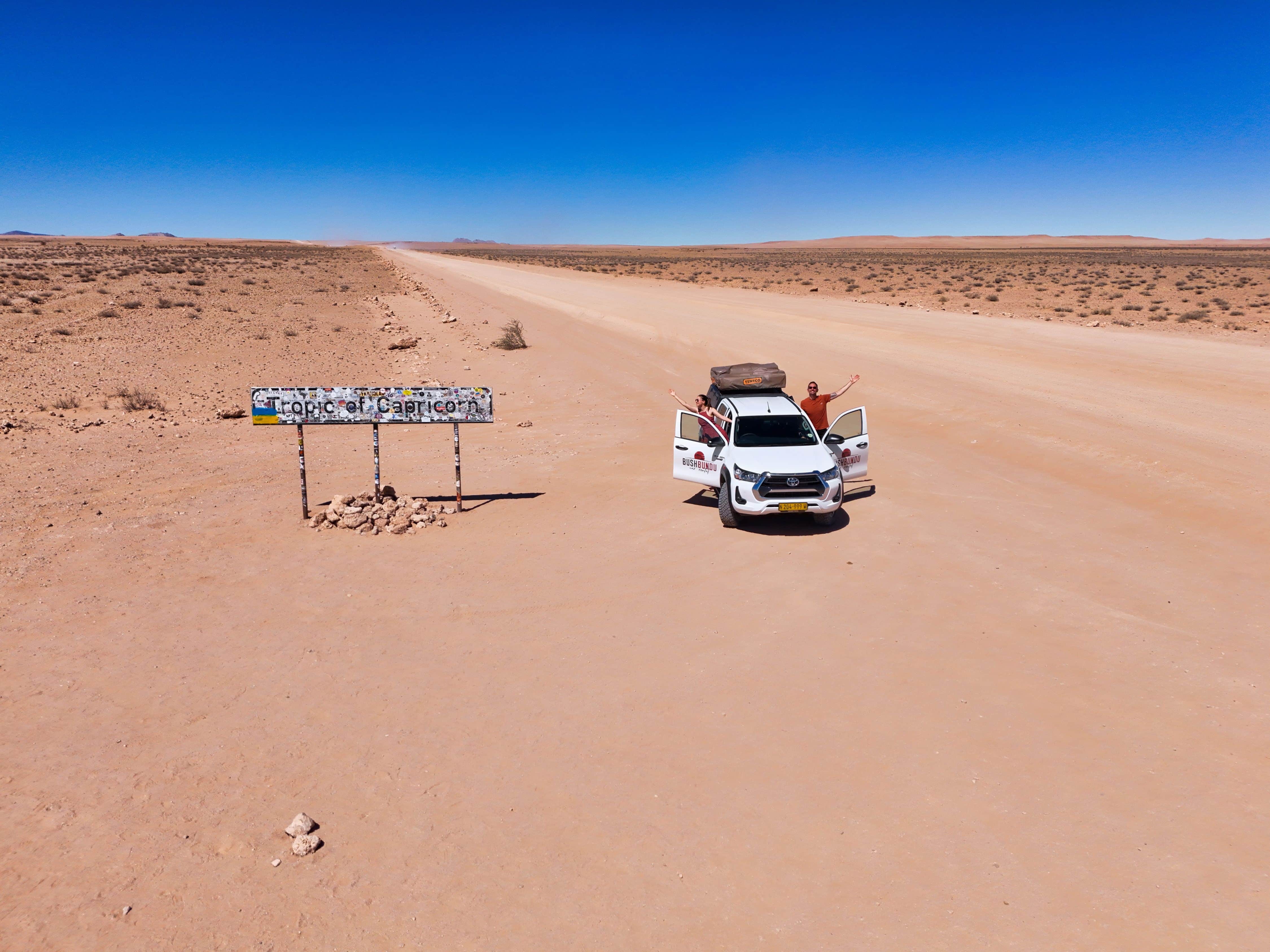 Couple heureux dans un 4x4 levant les bras au ciel au milieu d'une route désertique