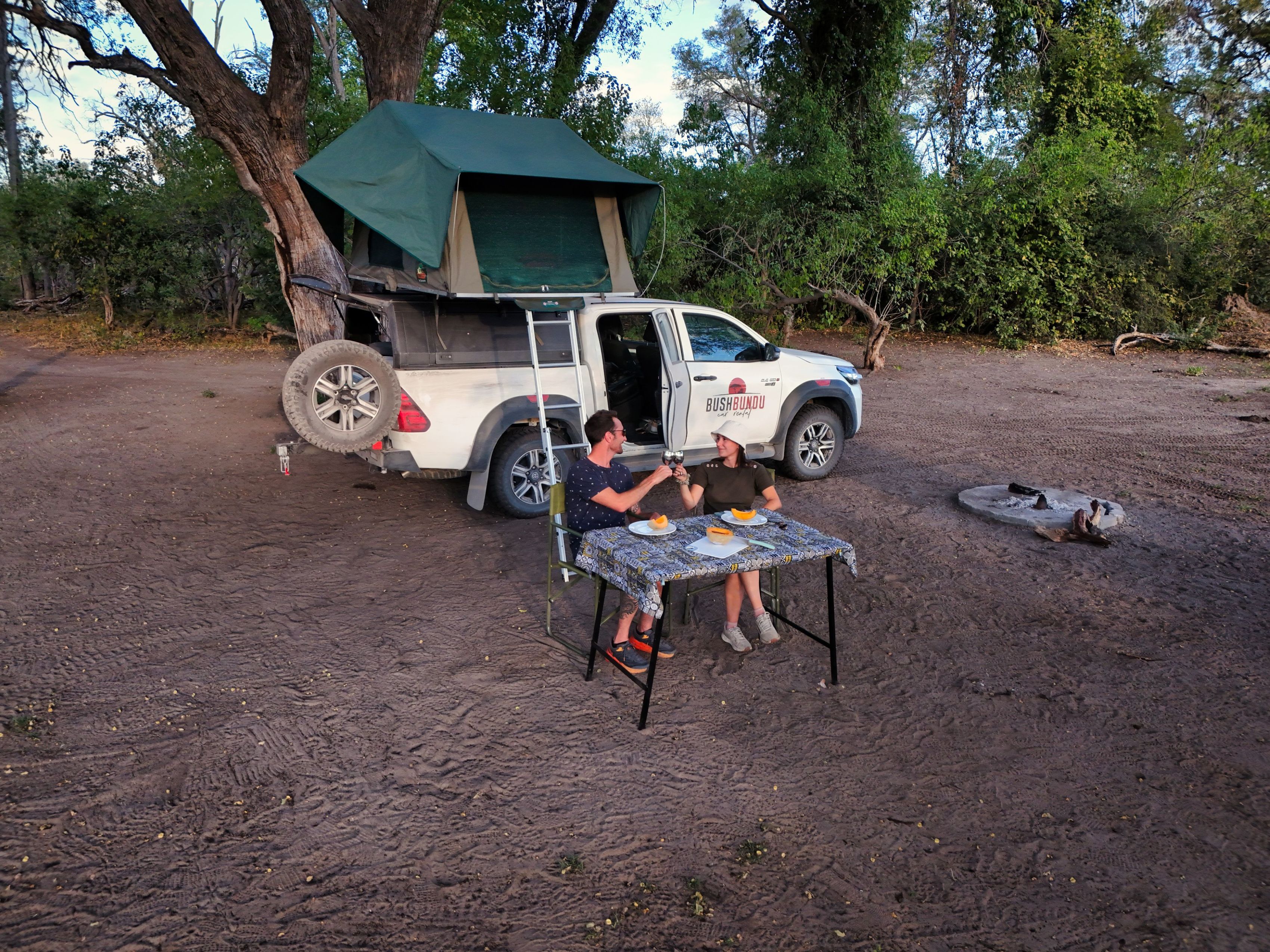 Couple qui trinque sur une table de camping devant leur 4x4