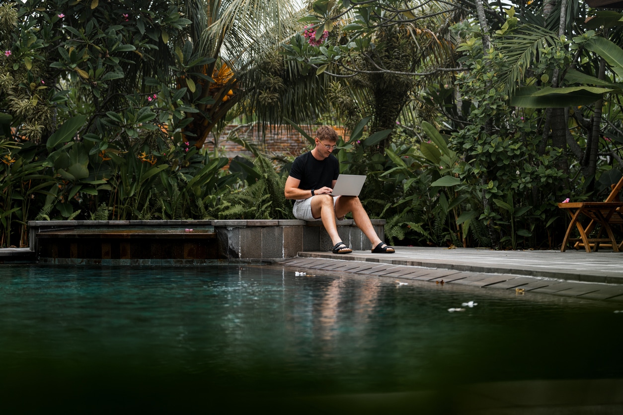Jeune homme travaillant sur son ordinateur au bord de la piscine