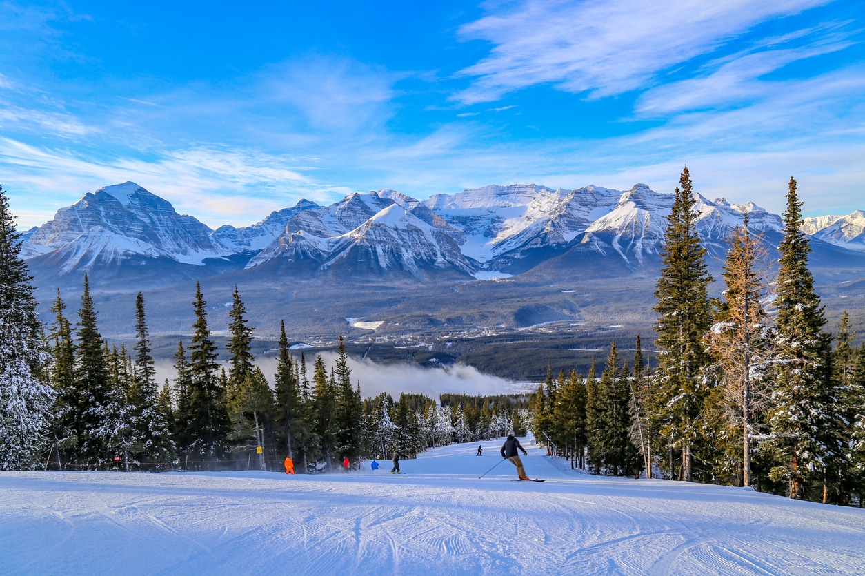 Skieurs qui descendent la piste de ski face à une chaîne montagneuse
