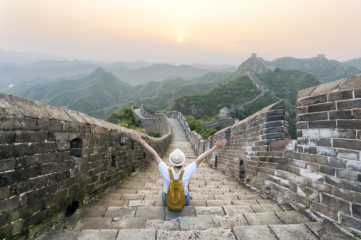 Jeune femme assise sur la grande muraille de Chine levant les bras vers le ciel 