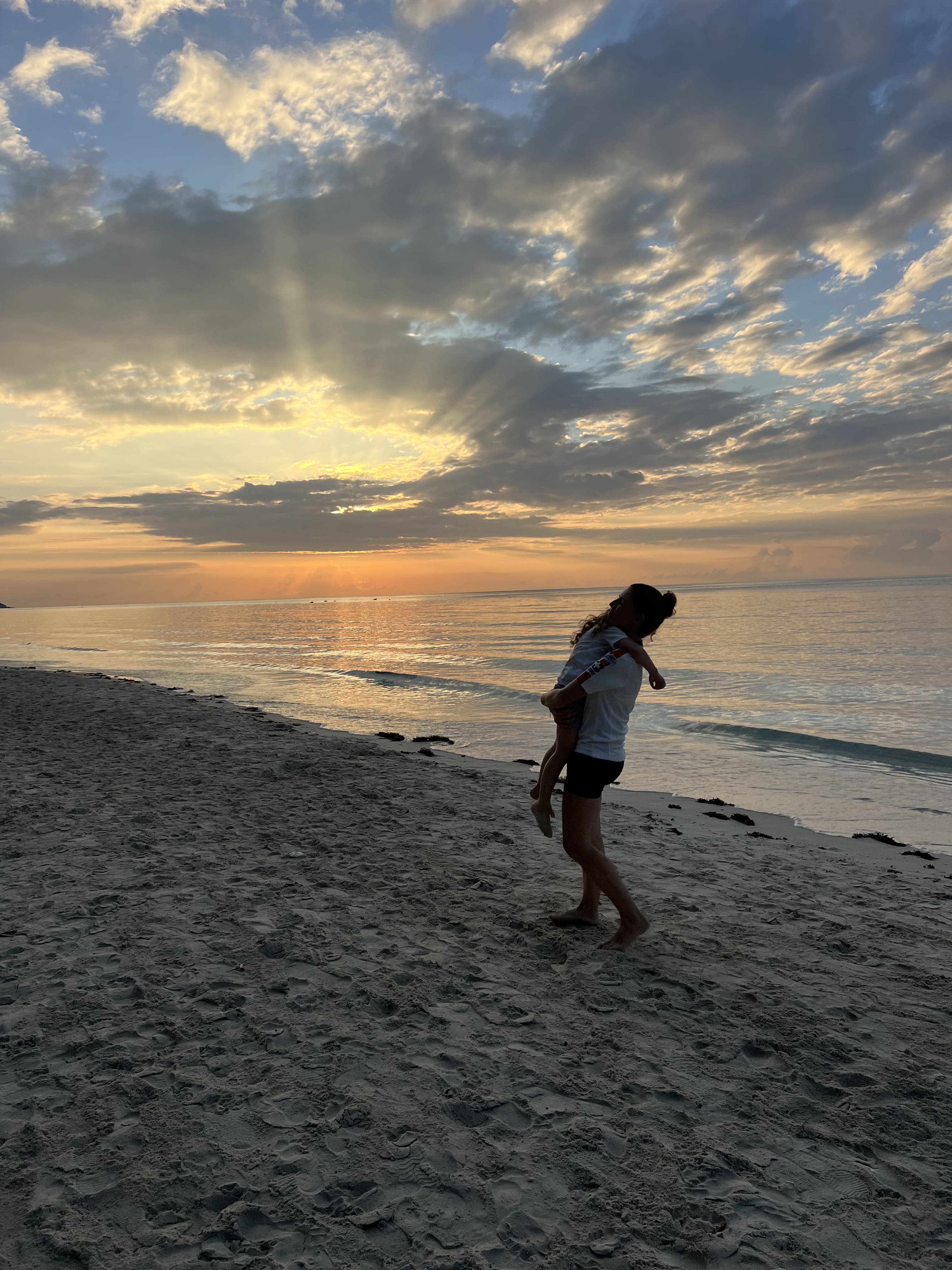 Maman qui tient sa fille dans ses bras sur la plage au coucher du soleil